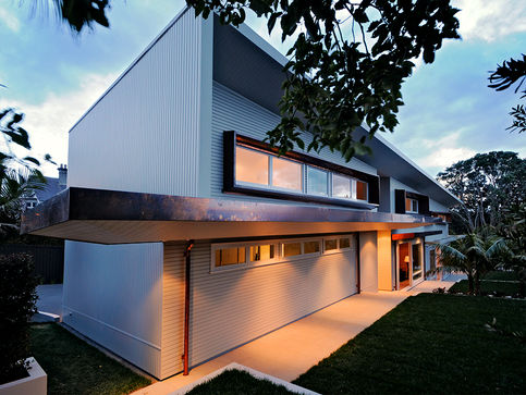 Modern corrugated metal-clad building with contemporary architectural design, exterior wall lighting, palm trees and a paved driveway.