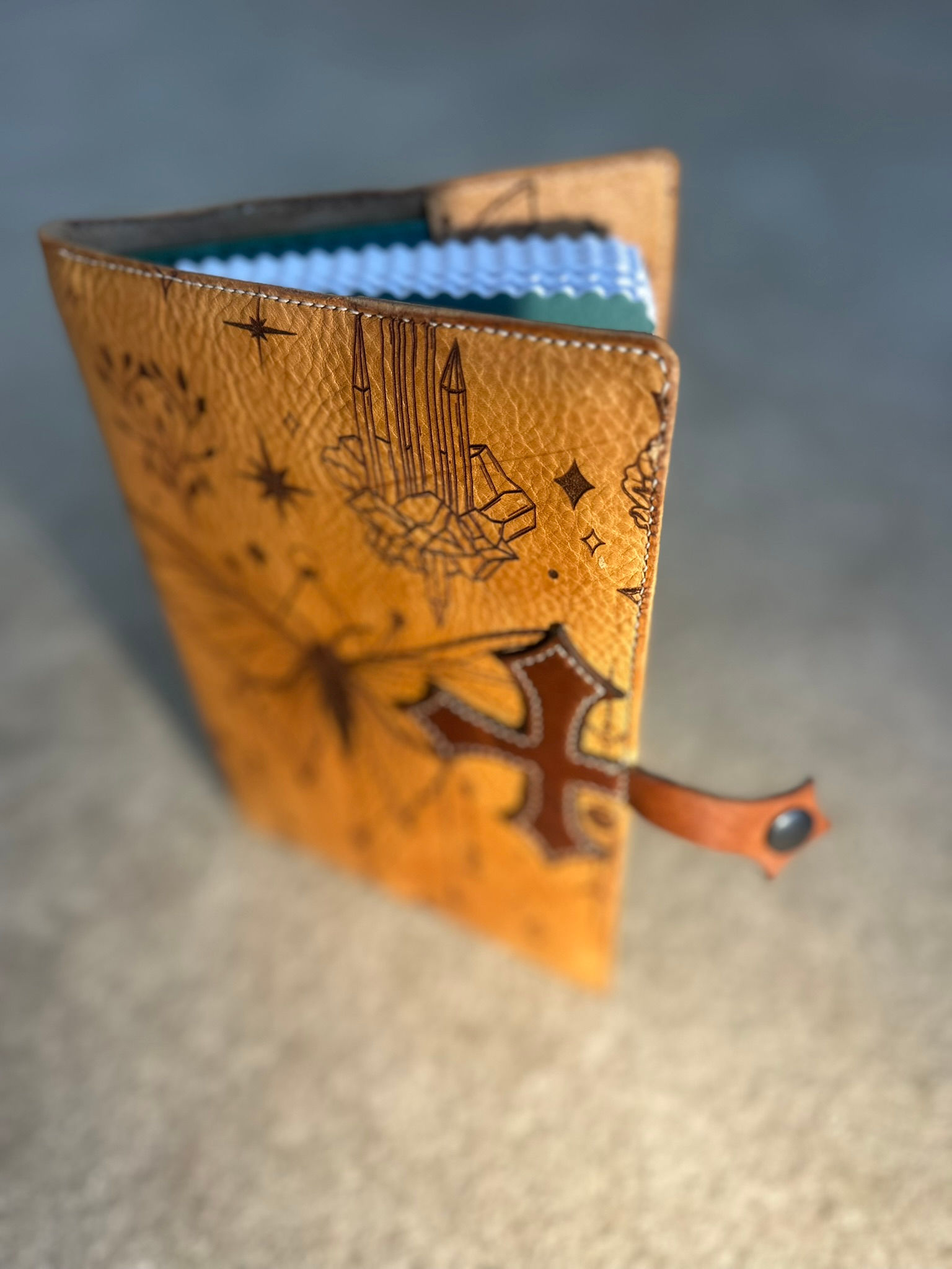 Voorkant van handgemaakte leren A5 notebook cover met gegraveerde vlinder, symbolen en kruisdetail.
