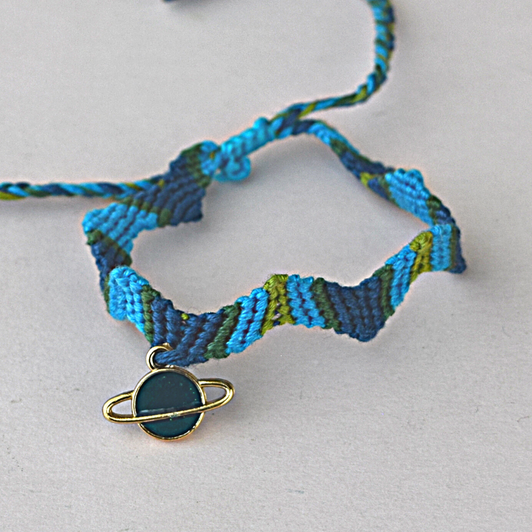 pulsera tejida en tonos azules y verdes con dije de planeta turquesa