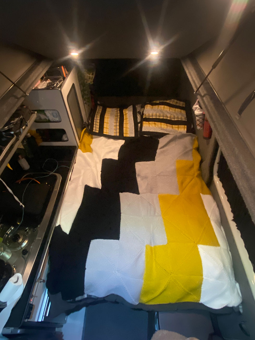 Cozy camper van interior with a geometric-patterned quilt in black, white, and yellow. Soft lighting sets a warm, inviting mood.