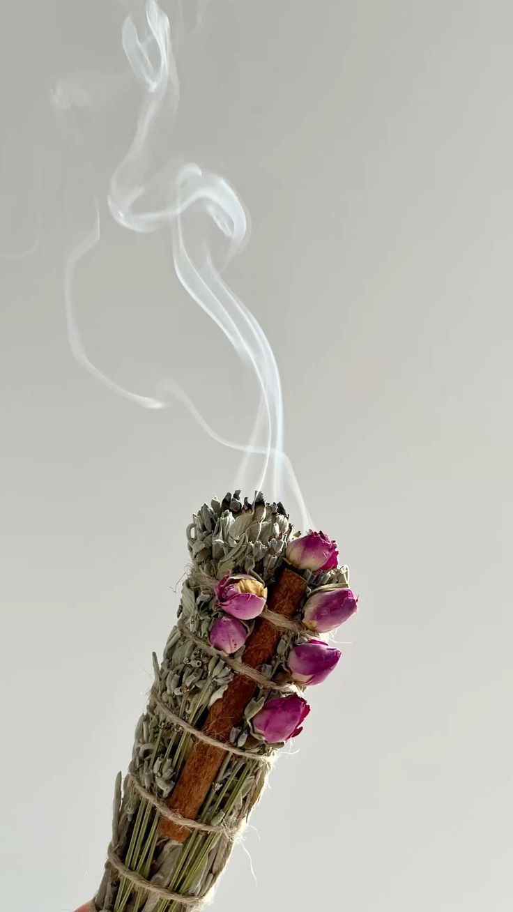 Smoking herbal cleansing bundle made with dried sage, rosebuds, and cinnamon stick against a neutral background, used for spiritual cleansing and energy clearing rituals.