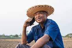Close-up of happy elderly male farmer talking on mobile phone while sitting on dry agricul