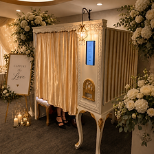 Elegant enclosed photo booth rental with cream curtains, vintage detailing, and white floral décor at a luxury wedding reception.