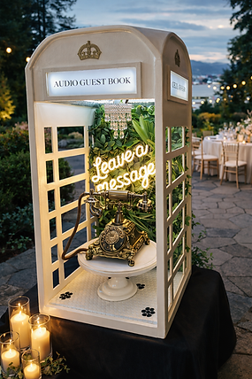 Elegant cream-colored audio guestbook phone booth featuring a vintage gold telephone, greenery backdrop, and glowing “Leave a message” sign, styled at an outdoor wedding reception at Cecil Green with candles, patio tables, and ocean view in the background.