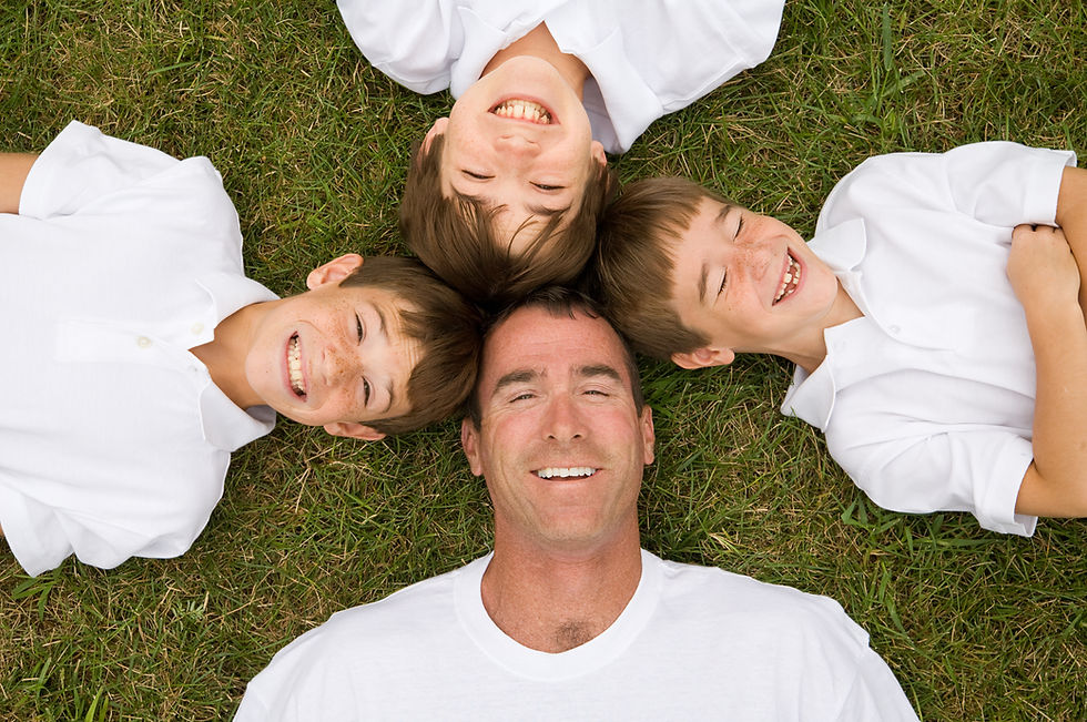Happy Dad and three sons laying on grass with top of heads together