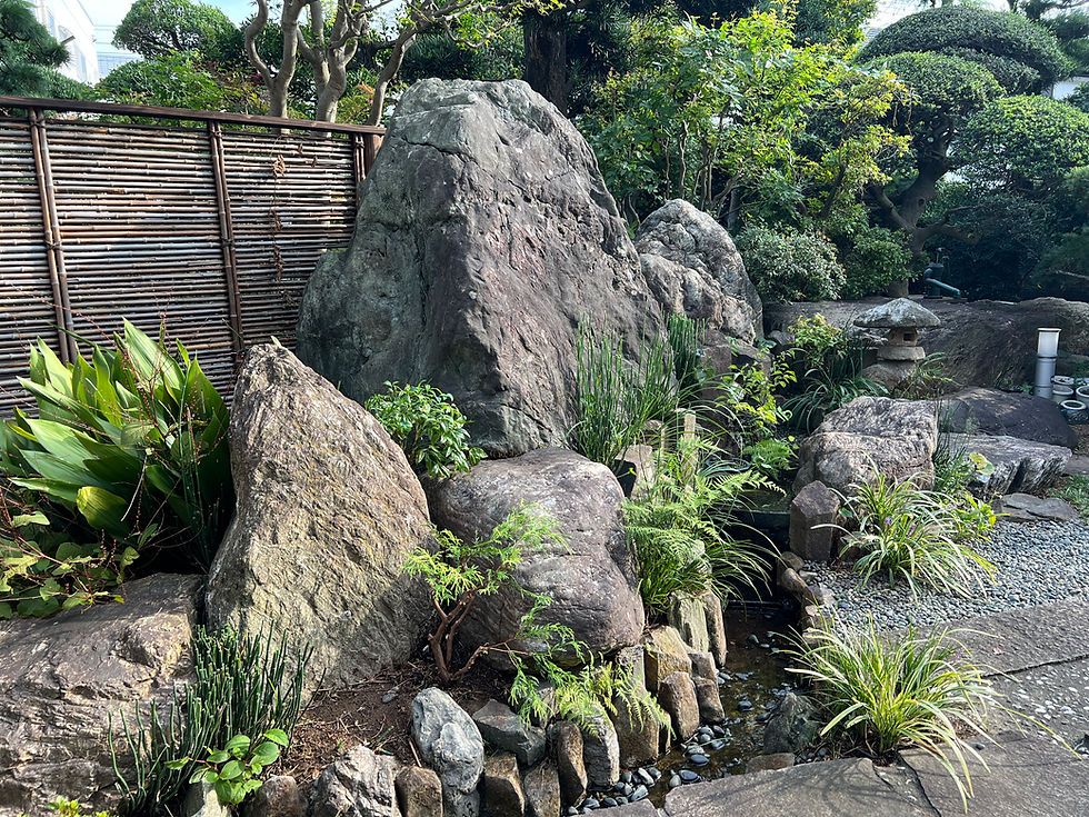 日本庭園の趣ある大きな石組みや飛び石、美しく手入れされた緑豊かな植栽や灯籠が配置され、自然の静けさと上品な和の空間が広がっている様子を示す画像です