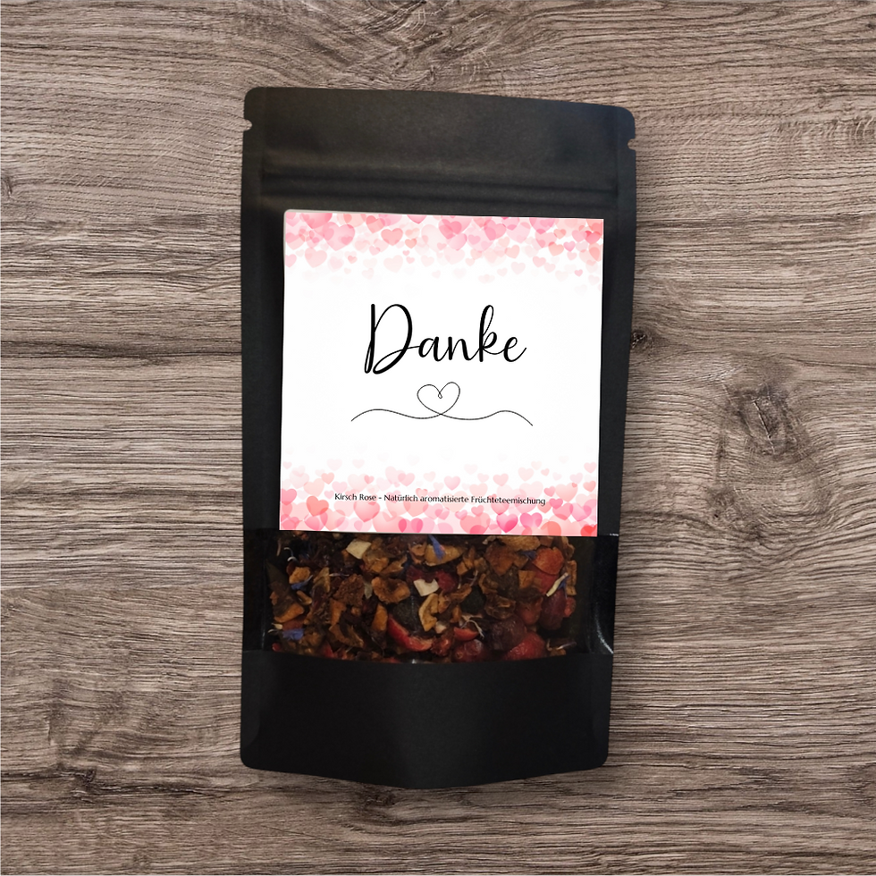 Miniaturbild: Tee in einer schwarzen, stehenden Verpackung mit Sichtfenster und Aufdruck "Danke" und mit rosa Herzen oben und unten.