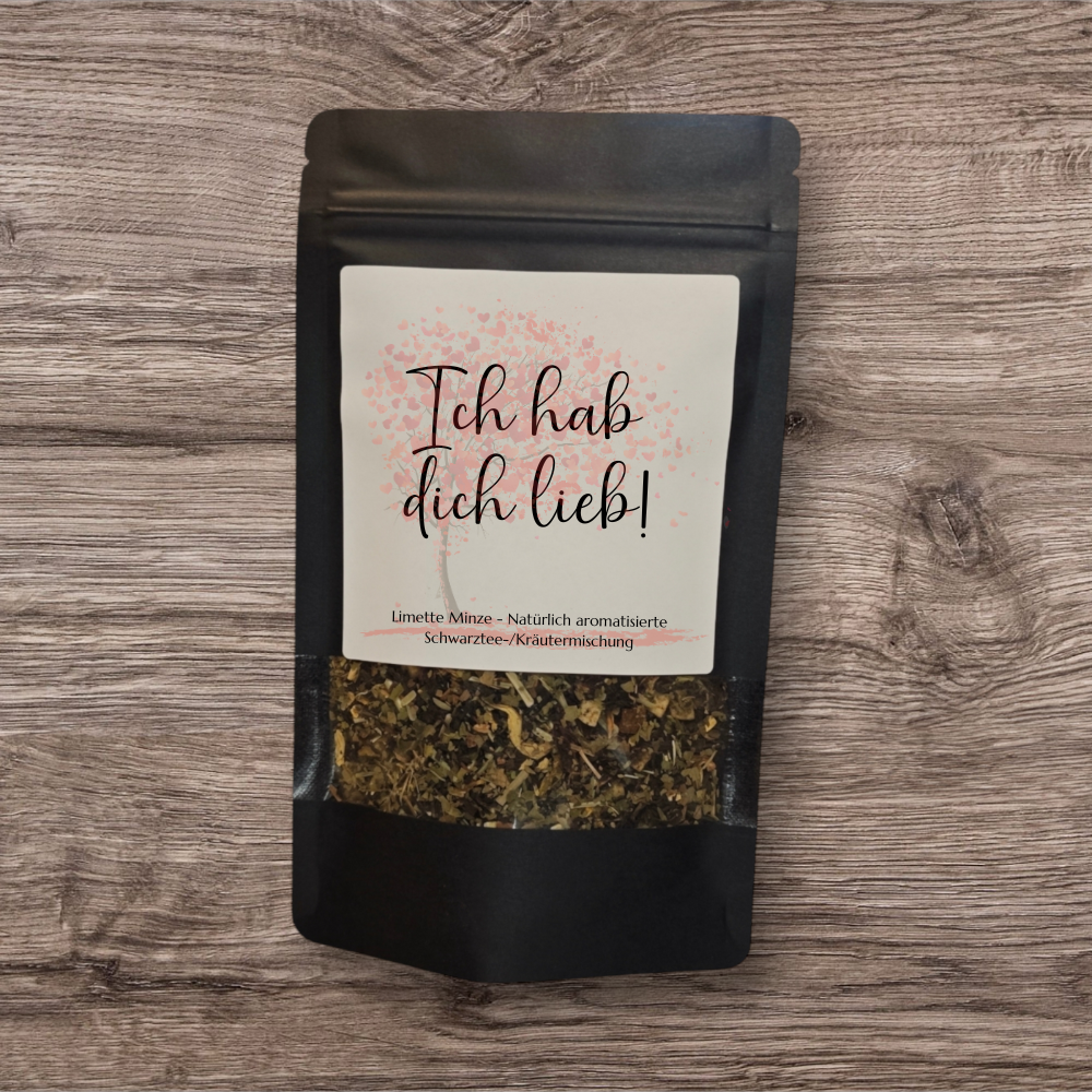 Tee in einer schwarzen, stehenden Verpackung mit Sichtfenster. Das Etikett trägt eine schlichte, elegante Gestaltung mit dem Schriftzug  'Ich hab dich lieb' in stilvoller Schrift und einem rosa Baum im Hintergrund. 