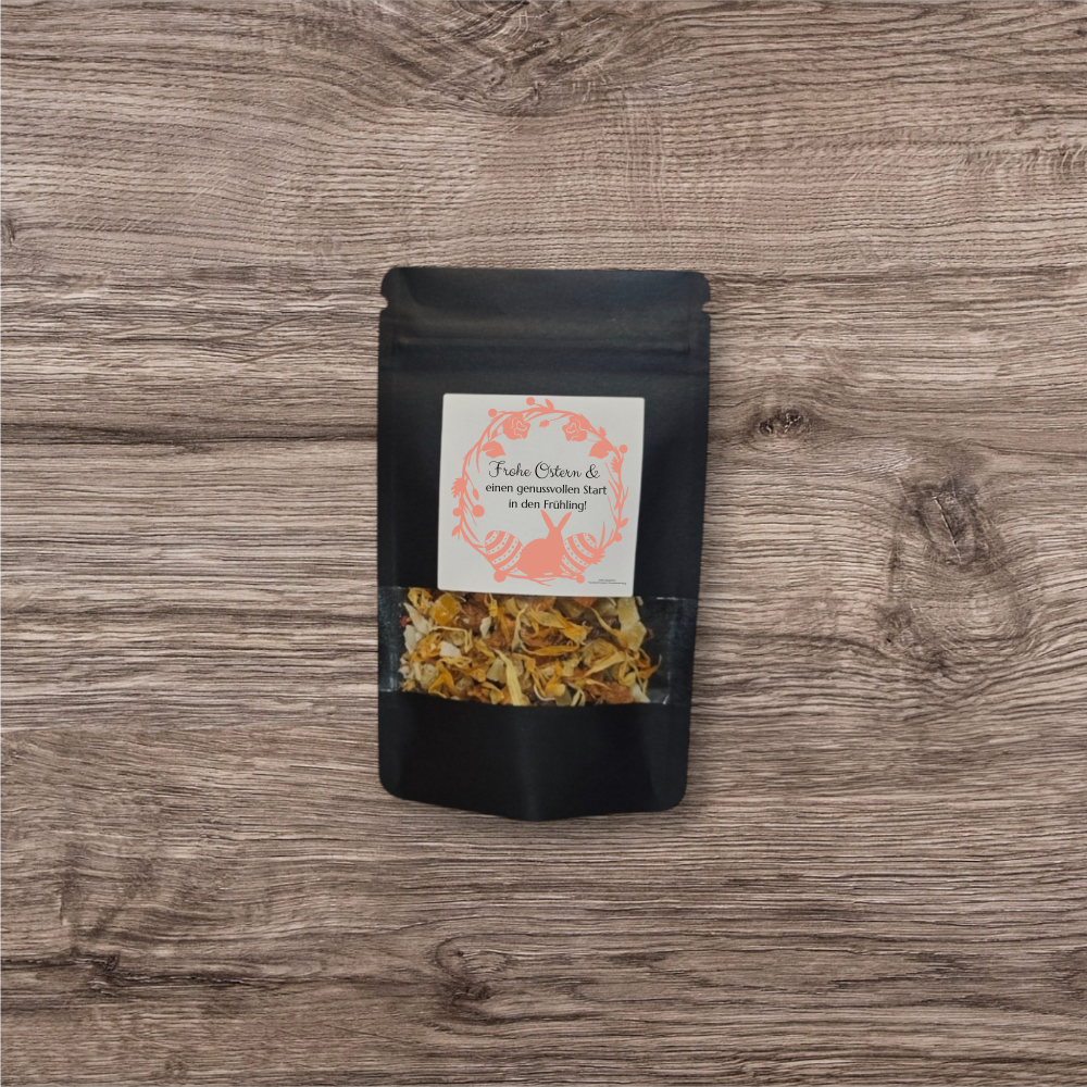 Tee in einer schwarzen, stehenden Verpackung mit Sichtfenster und Aufdruck "Frohe Ostern".