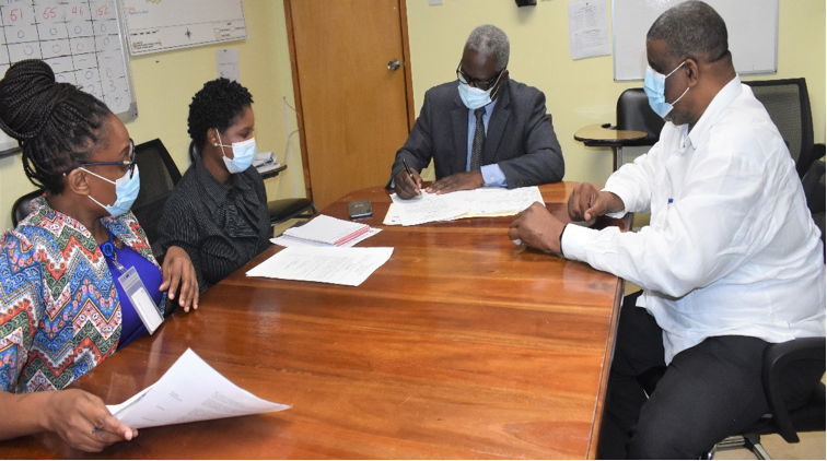 Mr. Wentworth Charles, Board Chairman, SERHA, signs approval for the assumption of duties of Mr. Errol C. Greene to function in the capacity as the Regional Director, SERHA. The signing was held inside the boardroom at the Regional Office on Thursday, July 8, 2021. Looking on from left are: Ms. Pauline Roberts, Director of Human Resources and Industrial Relations, SERHA; Ms. Stacey-Ann Steele, Corporate Secretary/Legal Officer, SERHA and Mr. Errol C. Greene, OD, JP, RD, SERHA