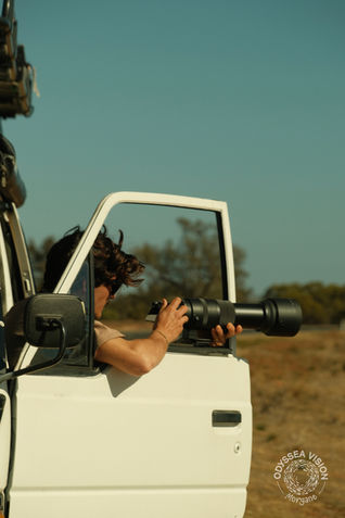 Photographer leaning out of a van door with a big lens, capturing shots outside.