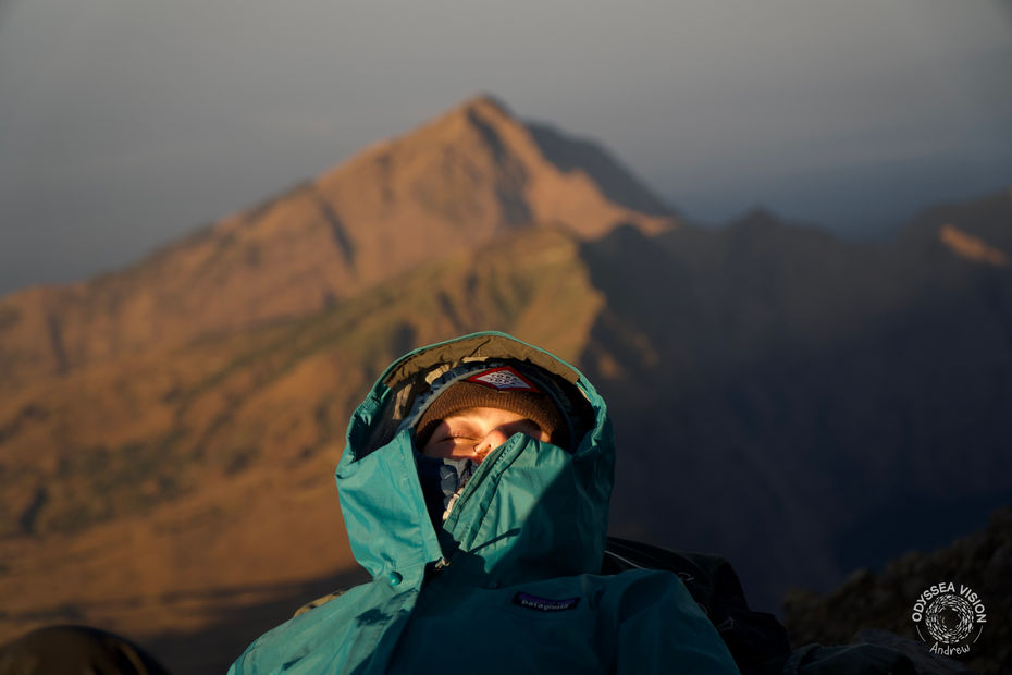 Adventurer resting at the summit of Mount Rinjani, a volcano on Lombok, Indonesia, with expansive volcanic terrain and scenic views in the background.