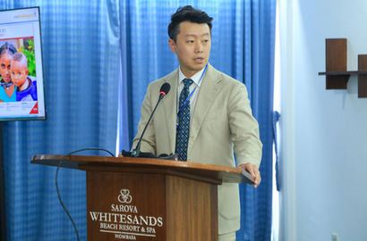 A speaker stands behind a lectern presenting to an audience.