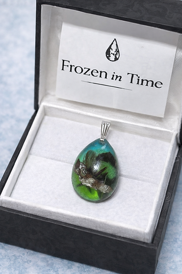 Oval memorial resin pendant with green and gold tones on handwritten paper background