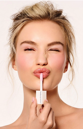 Model applying soft pink lipstick to create a natural makeup look