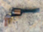 Revolver with a polished wood grip and brass accents set on a textured stone surface. "John Linebaugh" engraved on the cylinder.