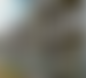 Construction site of modern apartment buildings with scaffolding, surrounded by fencing. Overcast sky, grey façade with visible insulation spots.