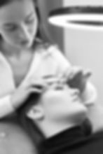 beautician with tweezers makes eyelash extension for young woman in beauty salon._edited.j