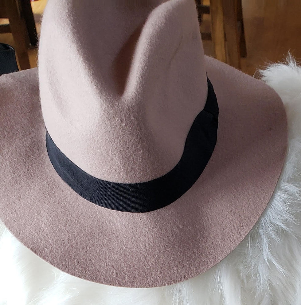 Light brown felt hat with black band on white fluffy surface