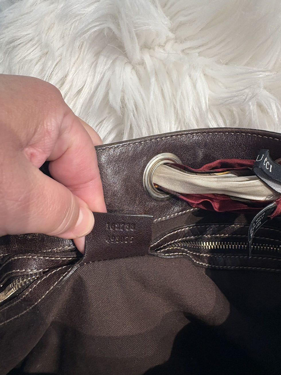 Thumbnail: Hand holding brand tag inside brown leather bag