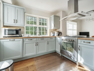 Light blue shaker kitchen with wooden worktops and large windows creating a bright family space.