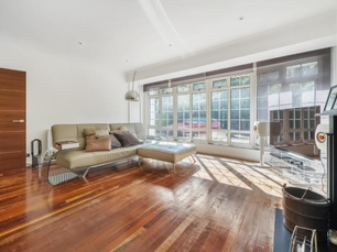 Bright open-plan living room with large windows, wooden flooring and neutral furnishings.