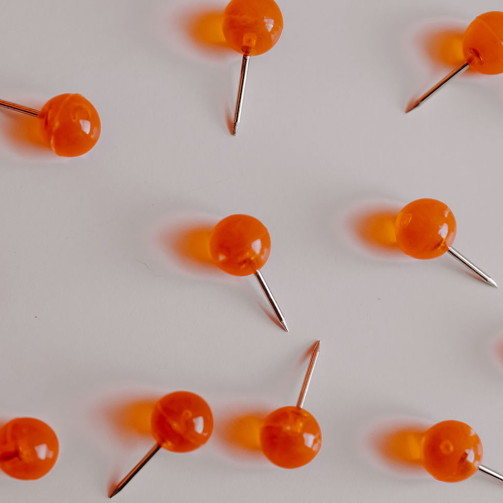 Scattered orange push pins on a white surface, with metallic points and soft shadows in a minimal abstract arrangement