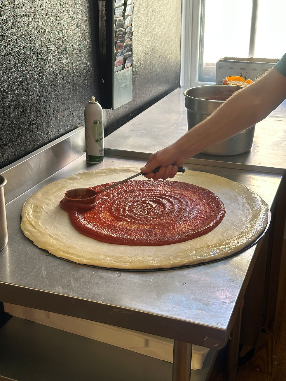 making a pizza in a commercial kitche, dough and now hand applying sauce