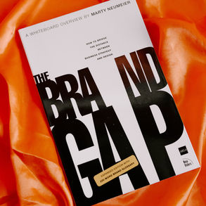 Book titled "The Brand Gap" by Marty Neumeier on orange satin. Features bold black and white text with a note about an expanded edition.