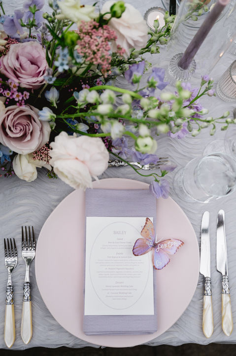 Shades of lavender floral wedding centerpiece and table setting details with charger, flatware, custom menu and butterfly decor
