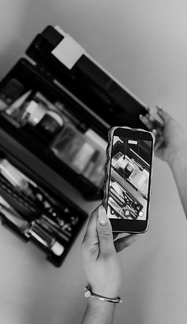Makeup In A tackle Box, A Hand with long nails holding an iphone taking a photo of the makeup in the tackle box, hand has a bracelete on, photo is in Black and White