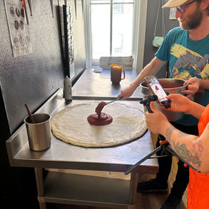 Pizza being created on silver kitchen with someone capturing content on iphone