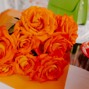 Orange Roses wrapped in orange paper next to a lime green purse with a short strap