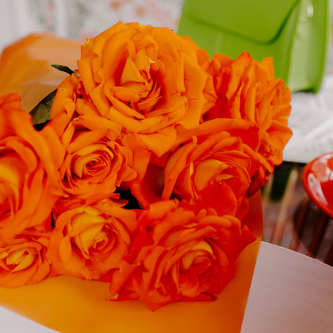 Orange Roses wrapped in orange paper next to a lime green purse with a short strap