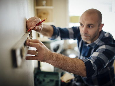 Mature man using a spirit level and marking the wall with a pencil in his kitchen..jpg