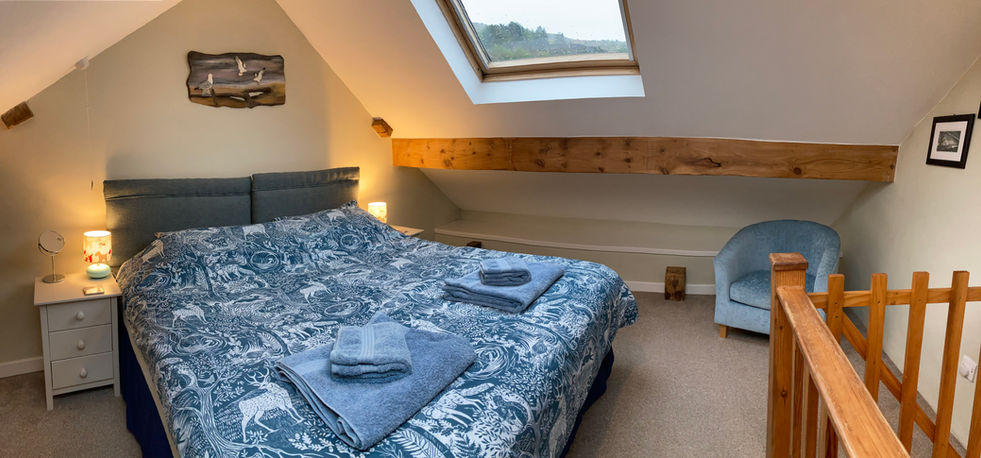 The bedroom at Bryn Meurig Bach holiday cottage, with a king size bed and skylights above the bed to look out at the Wales Coast Path and the night sky in Snowdonia's Dark Skies Reserve.