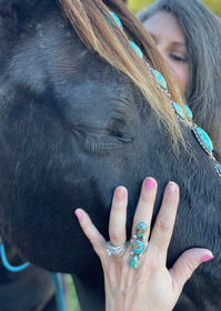 zoomed in image of a black horse's face with lady's hand featuring a turquoise ring 