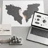 Top-down view of a modern desk with a map showing nearshore connections between regions, two concrete city models linked by a bridge, and a laptop displaying IT consulting workflow diagrams, representing nearshore IT consulting collaboration