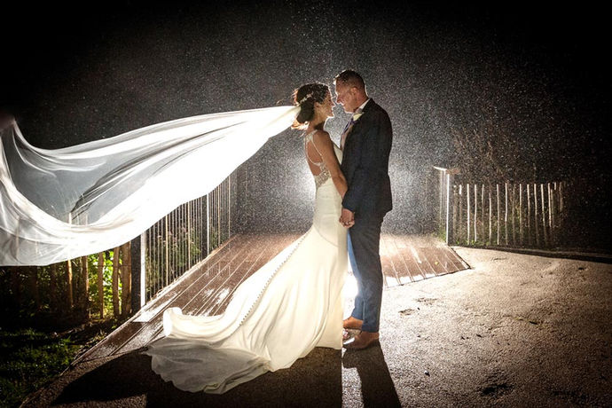 a bride and groom stand backlit together at night in the rain with her veil blowing on Inchydoney beach