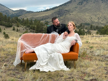 Couple poses on orange couch, bride in dress, mountains in background, The Copper Lodge
