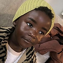 Young person in yellow hat smiles at camera with zebra print jacket.