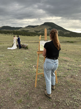 Artist painting a wedding scene; couple with mountain background on cloudy day