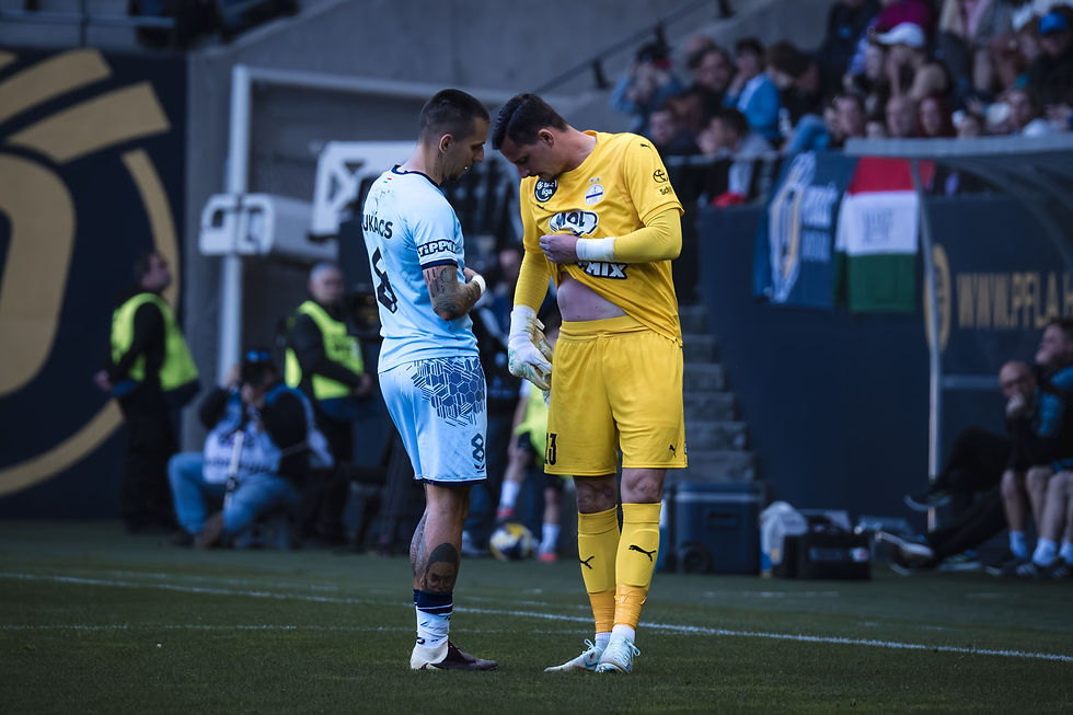 El portero del Újpest FC enseña el lugar de su lesión al jugador Dániel Lukács del Puskás Akadémia. Foto: (Javier Zambrano).