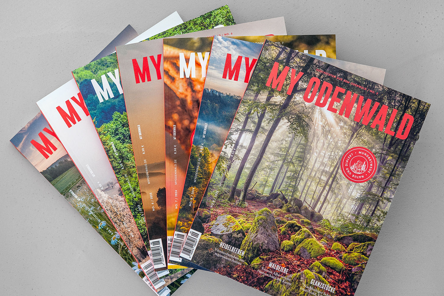 MY ODENWALD Magazin-Set,  Ausgaben 3-9: Also sieben Magazin-Hefte. Die Magazine sind aufgefächert auf einem grauen Untergrund fotografiert. Das Magazin Nr. 9 liegt oben.
