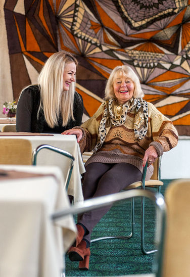 Zwei Frauen lachen, entspannter Plausch im Hotel vor 70er Jahre Teppisch an der Wand