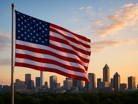U.S. flag waving against a city skyline at sunset. The sky is orange with scattered clouds, creating a patriotic and serene atmosphere.