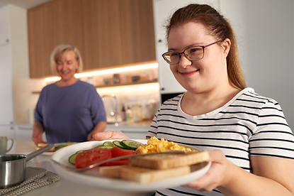 Participant preparing and serving a meal with support nearby at home
