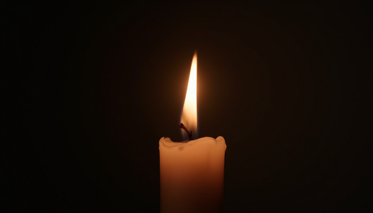 Eye-level view of a single candle burning steadily in a dark room