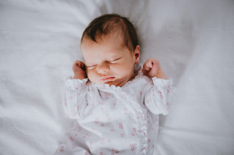 Beautiful newborn baby girl photographed in a simple white and pink babygrow on a clean white background.