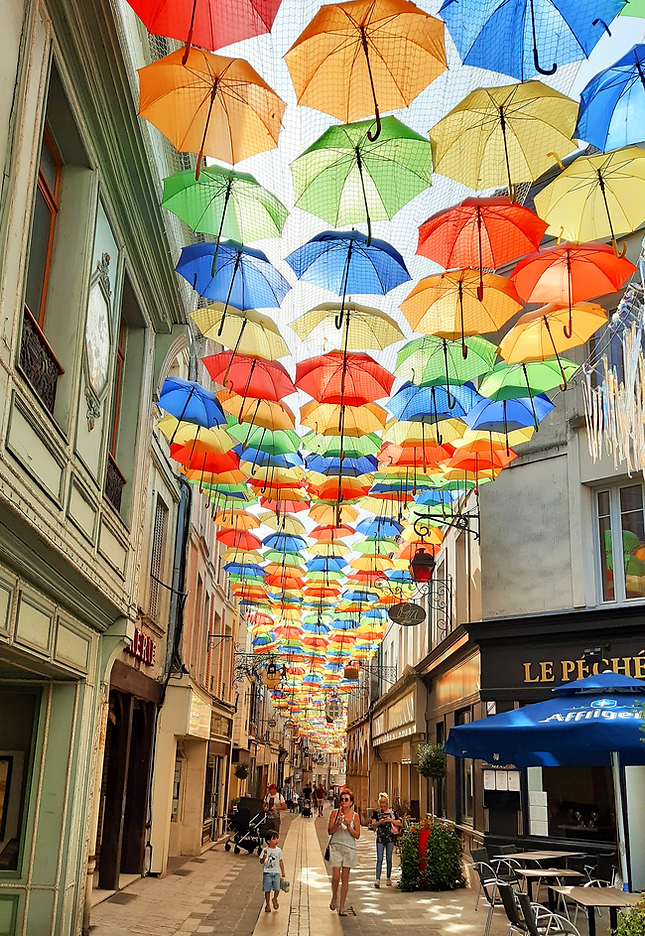 Artistic photo of narrow street in a French town with an art installation of coloured umbrellas overhead